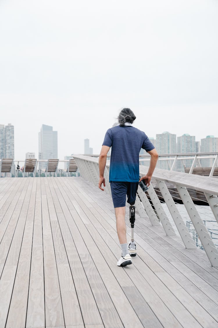 Back View Of Man With Prosthetic Leg Walking On Footbridge 