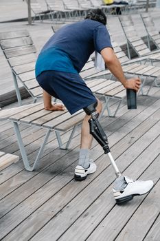 Man with a prosthetic leg sitting on outdoor seating, holding a bottle.
