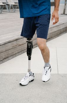 A close-up view of an adult male walking outdoors with a prosthetic leg on a sunny day.