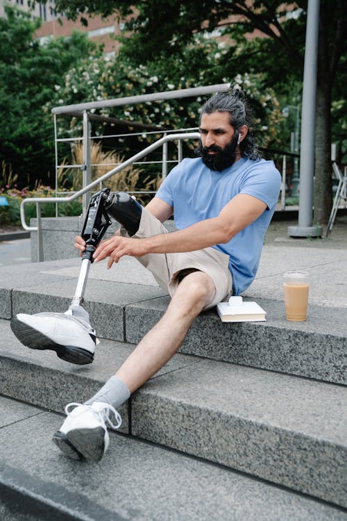 Man fixing his Prosthetic Leg seated on a Concrete Staircase