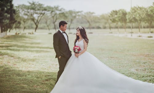 бесплатная Женщина в свадебном платье стоит рядом с мужчиной в смокинге Стоковое фото
