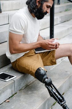 Man with a prosthetic leg seated on stairs writing in a notebook, demonstrating focus and determination.