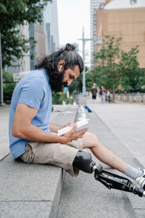 Free Man with a prosthetic leg focused on reading a book outdoors. Stock Photo