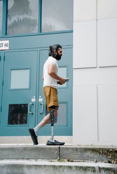Side view of a young man with a prosthetic leg walking past a building, displaying confidence and determination.