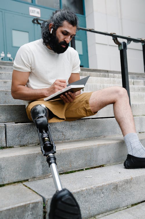 Man with Prosthetic Leg sitting on Stairs reading Book 