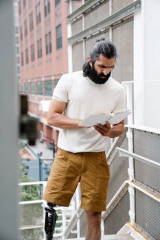A man with a prosthetic leg engrossed in reading a book on an outdoor stairway.