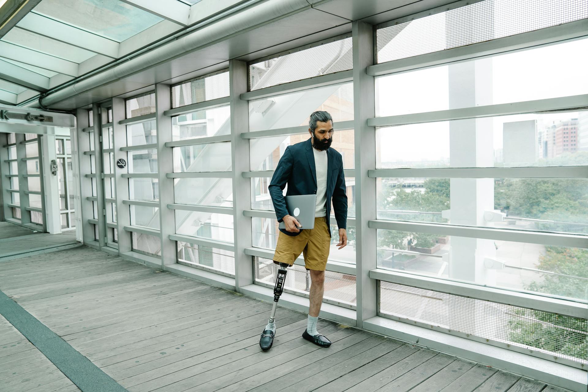 Young man with prosthetic leg confidently walking in a modern indoor walkway, embracing body positivity.