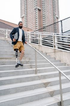 Confident businessman with prosthetic leg in urban setting, holding a laptop while descending stairs.