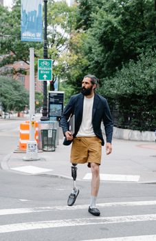Man with a prosthetic leg walking confidently on a city street near Hudson River.