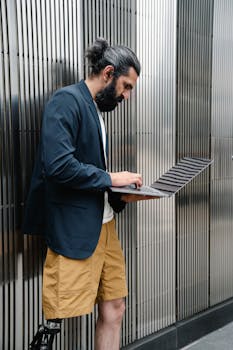 Focused man with prosthetic leg working on laptop indoors wearing a blazer and shorts, exemplifying modern work style.