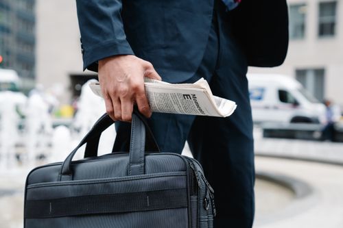 Free Close-up of businessman in suit holding a briefcase and newspaper in urban setting. Stock Photo