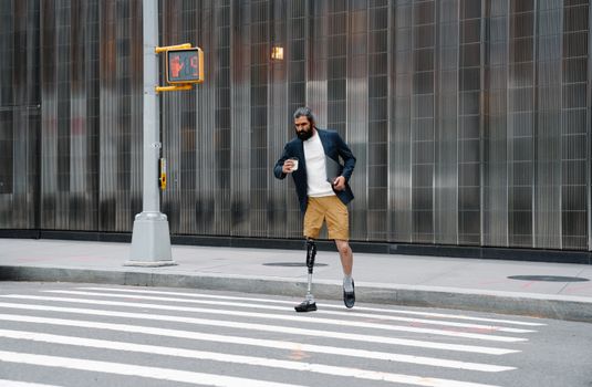 Confident man with prosthetic leg in urban setting holding coffee and tablet.
