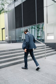 Professional man in formal attire ascending stairs outside a modern office building.