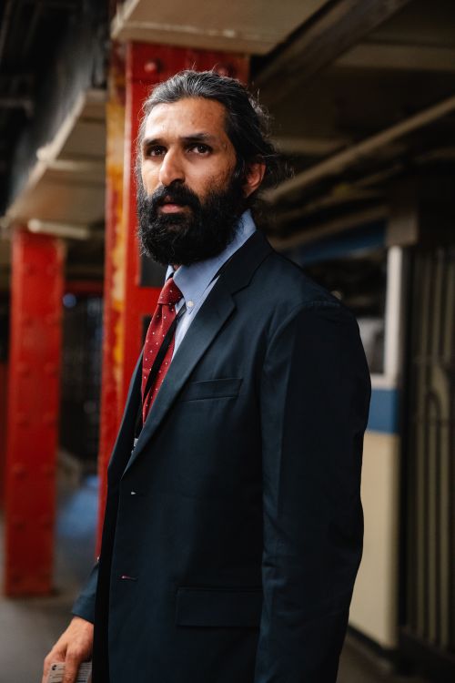 Free A bearded businessman in formal attire standing in an underground station, looking away thoughtfully. Stock Photo