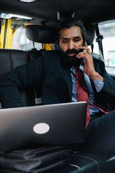 Professional man in a taxi working on laptop and talking on phone.