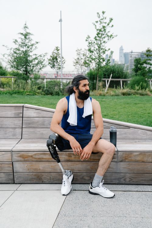 Free Man with prosthetic leg sitting on a bench outdoors, exhibiting a healthy lifestyle and body positivity. Stock Photo