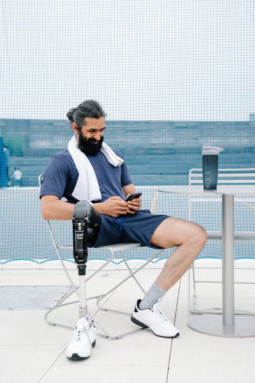 Man with Prosthetic Limb sitting on a Chair while Happily looking at Phone