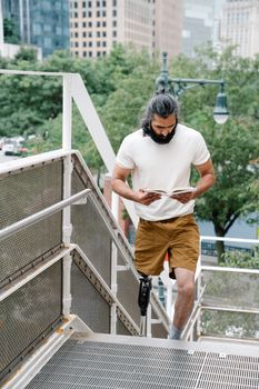 Adult man with prosthetic leg reads while ascending outdoor stairs.