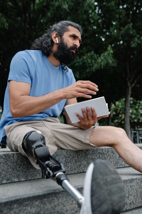 Free Man with prosthetic leg reading on outdoor steps, embodying resilience and focus. Stock Photo