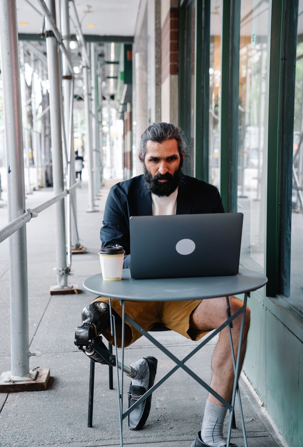 Hombre con prótesis de pierna trabajando con un computador portátil en un espacio exterior urbano.