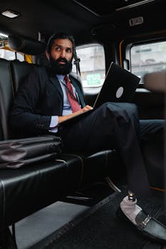 Professional businessman using a laptop inside a car, representing digital nomad lifestyle.