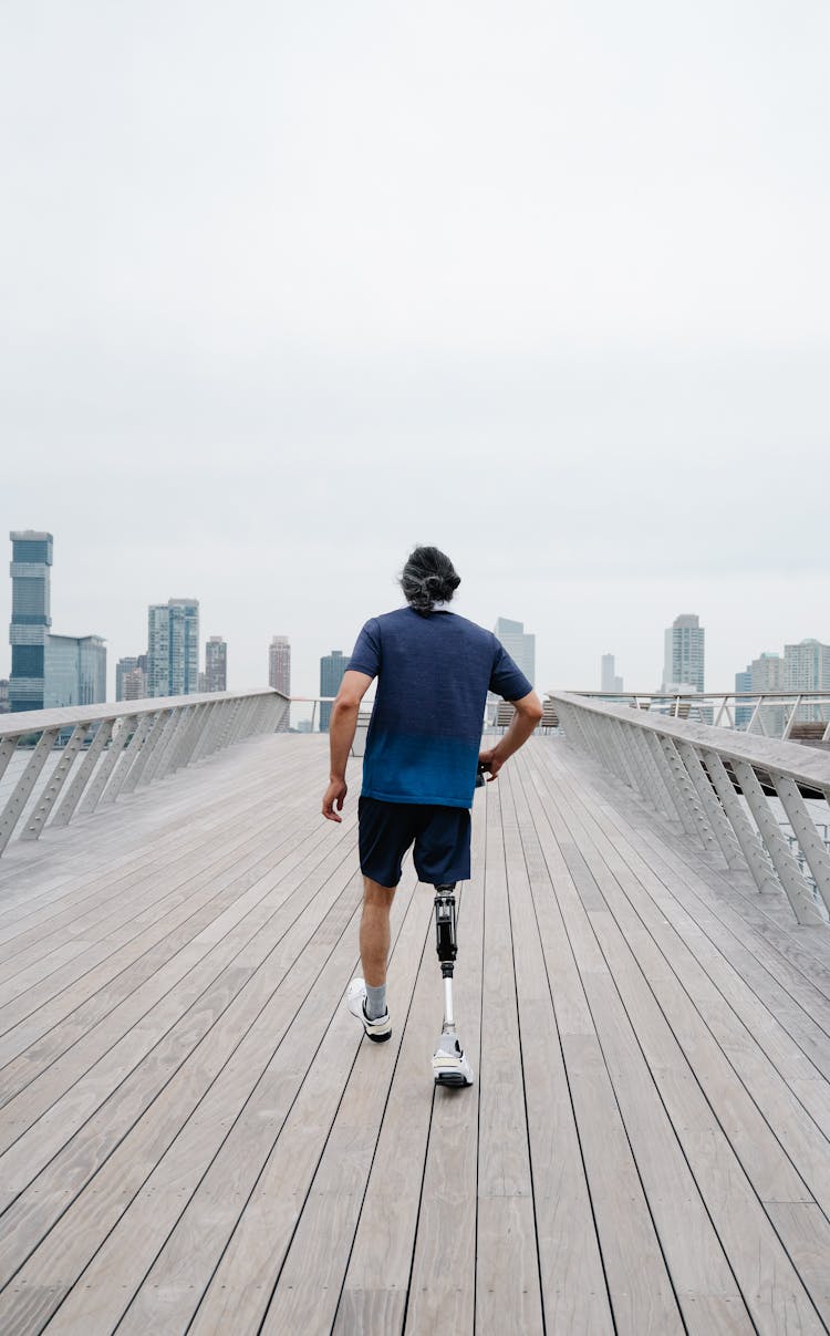 Man With Prosthetic Limb Walking On A Wooden Footbridge 