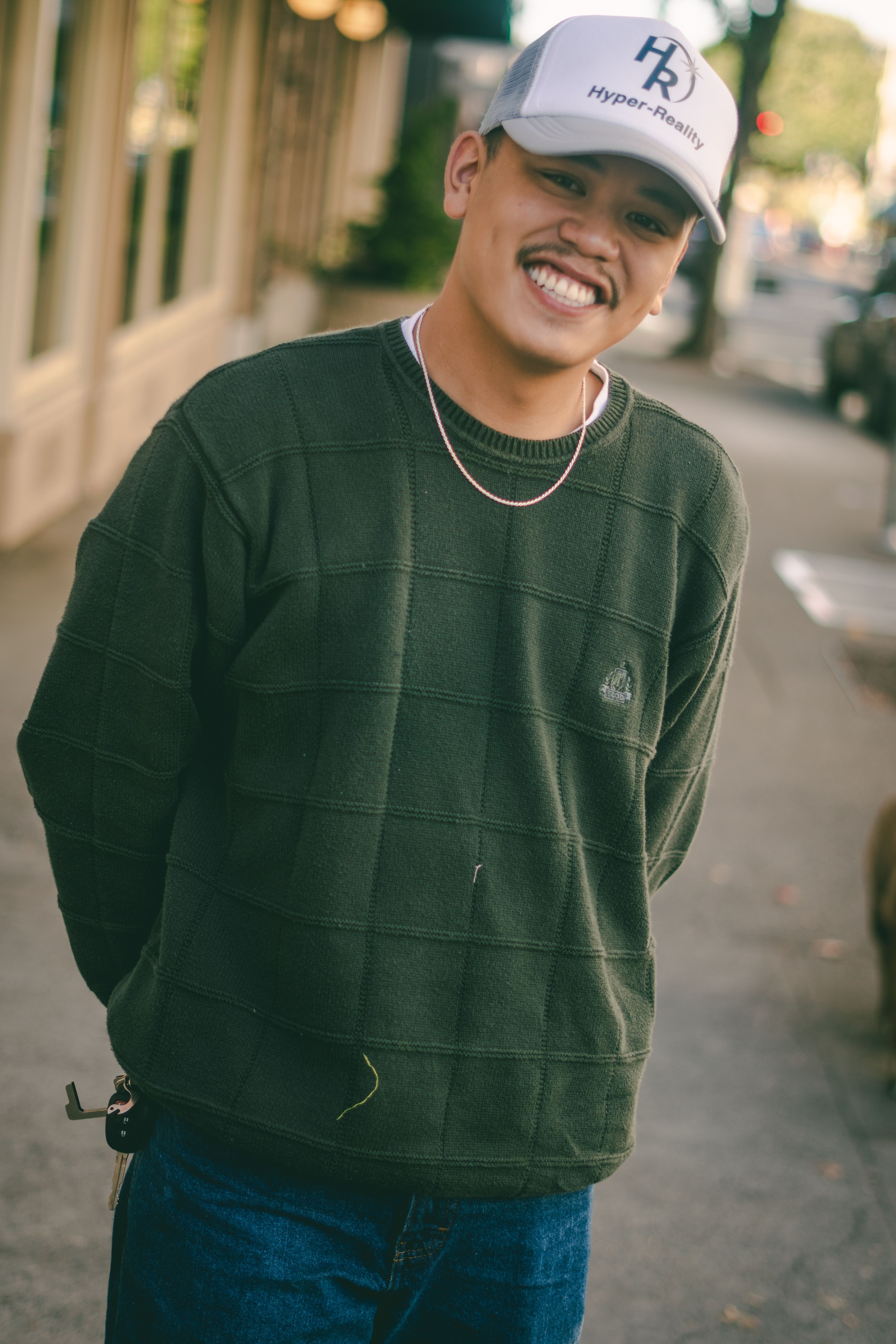A happy young man wearing casual streetwear smiles confidently on an urban street.