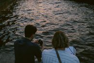 Two Men Sitting on Concrete Dock Holding Camera and Paper
