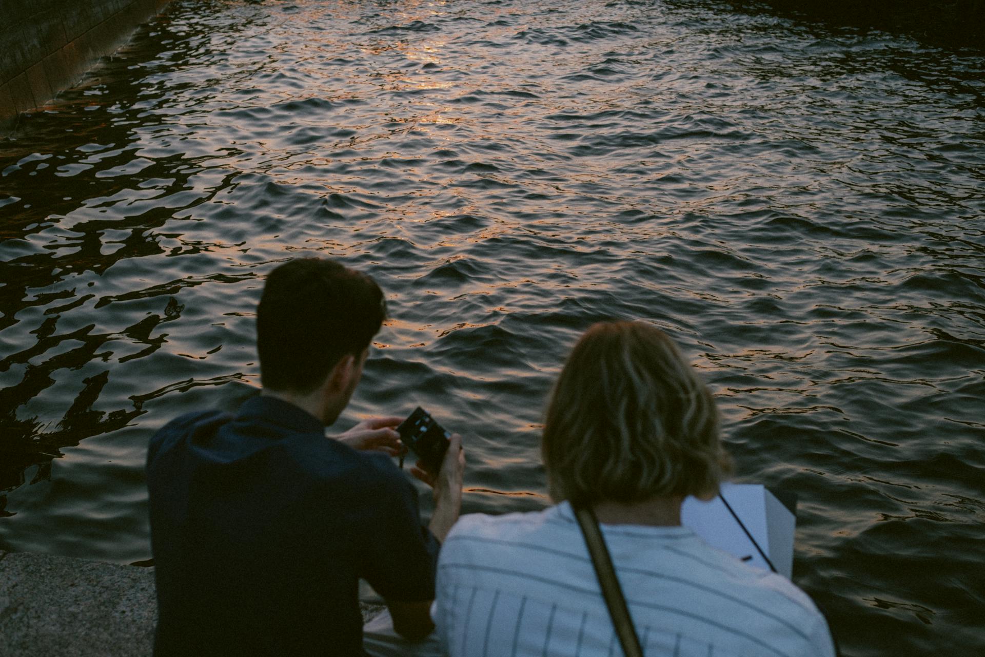 Two Men Sitting on Concrete Dock Holding Camera and Paper
