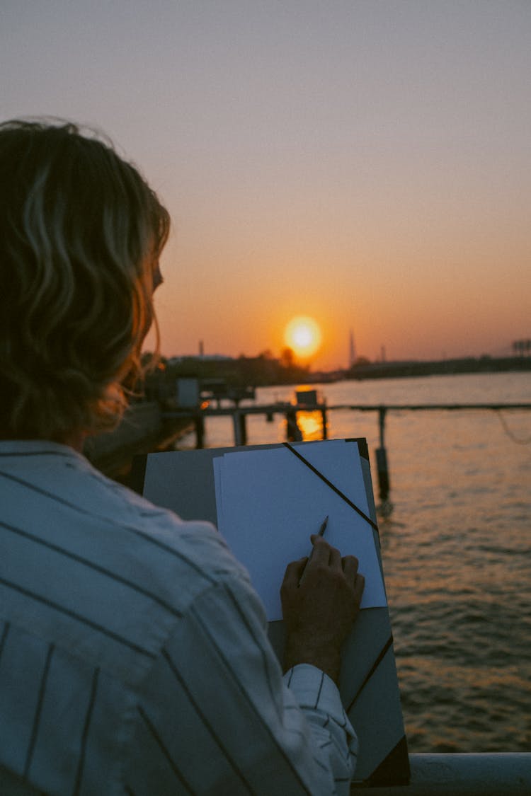 Blonde Man Writing By River At Sunset