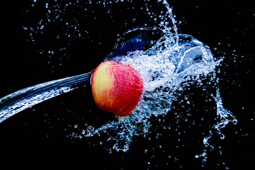 Close-up of a red apple captured mid-splash with water droplets against a black backdrop.