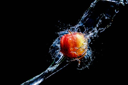 Close-up of a red apple splashing in water against a black background, capturing motion and freshness.