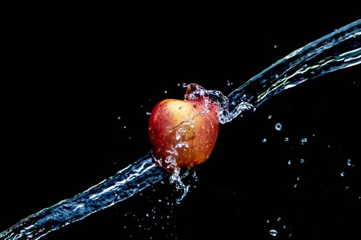 Close-up of a red apple splashing in water on a dark background.