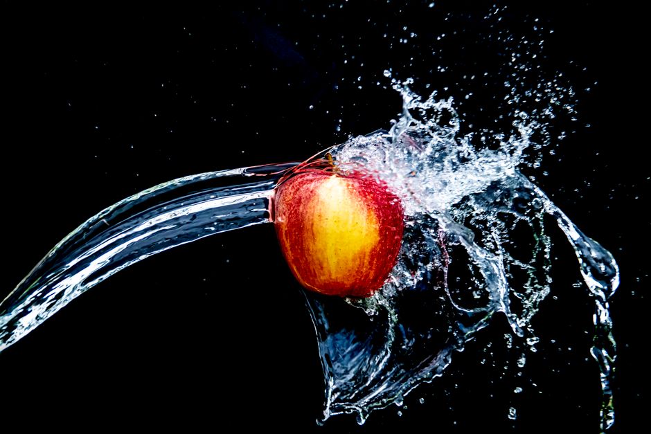 Red apple splashing in water against a black background, showcasing vibrant motion.