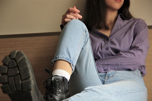 Close-up of a woman in denim jeans and striped shirt sitting casually indoors.