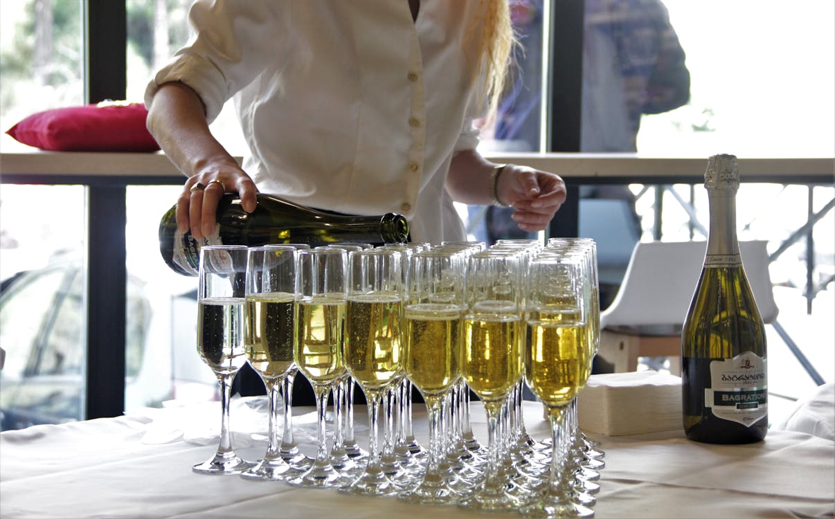 Free A woman pours champagne into glasses at an indoor event, creating a festive mood. Stock Photo