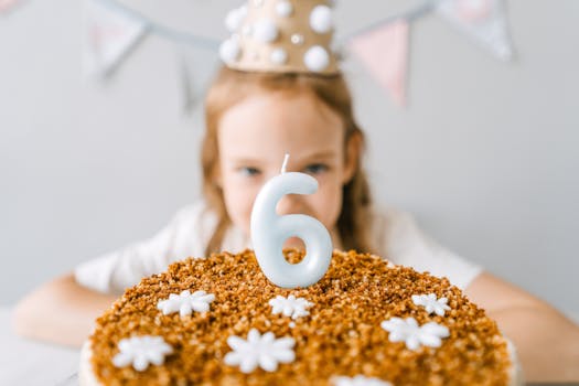 A young girl celebrates her 6th birthday with a cake featuring a number six candle.