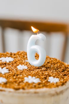 Close-up of a cake with a lit number six candle surrounded by decorative icing flowers.