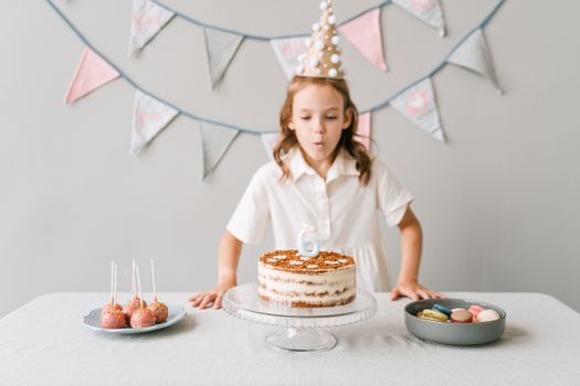 A young girl blows out candles on her birthday cake at a decorated indoor party.