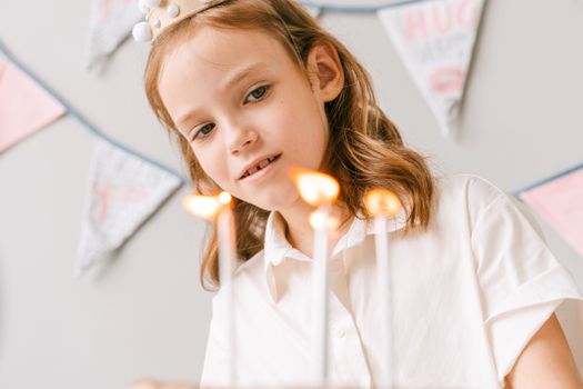 A young girl joyfully celebrates her birthday with candles on her cake indoors.
