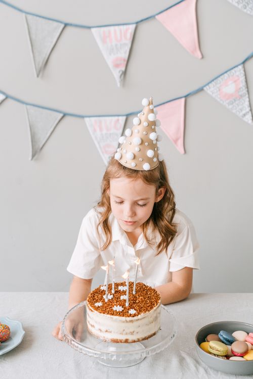 Free Young girl in party hat about to blow out birthday cake candles indoors. Stock Photo