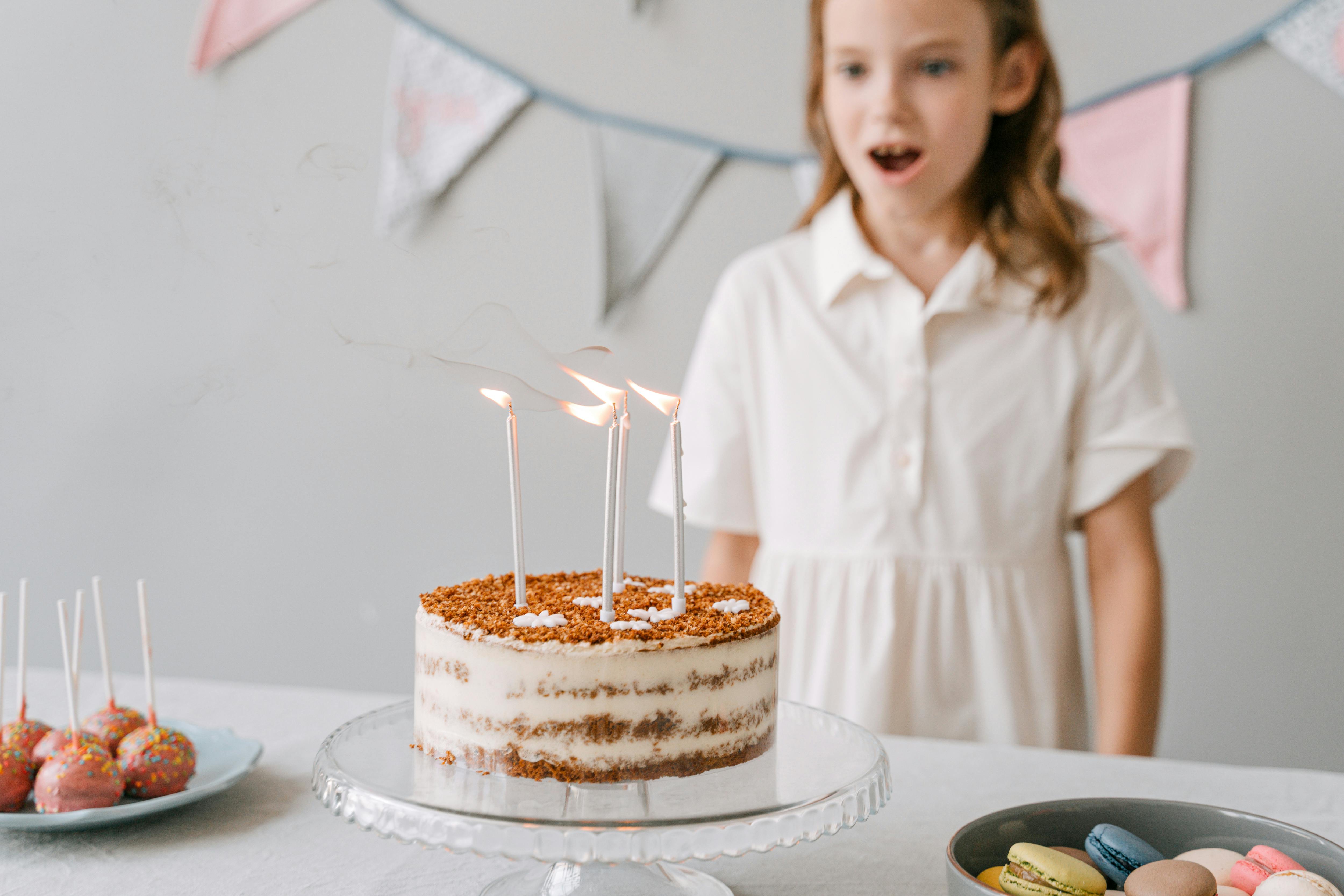A young girl is surprised and delighted in front of her birthday cake with lit candles, ready to celebrate.