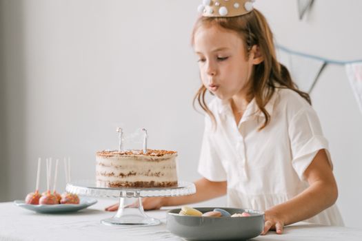 Young girl celebrates her birthday by blowing out candles on a cake, surrounded by treats.