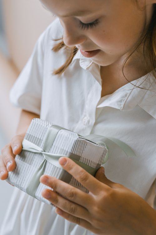 Free A close-up of a young girl in a white dress holding a beautifully wrapped gift box. Stock Photo