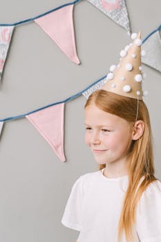 A smiling girl wearing a party hat stands in front of decorative bunting.