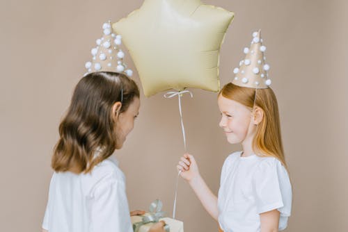 Photo of a Girl Holding a Balloon Near Another Girl
