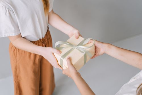 Free A close-up view of two people exchanging a gift box tied with a ribbon indoors. Stock Photo