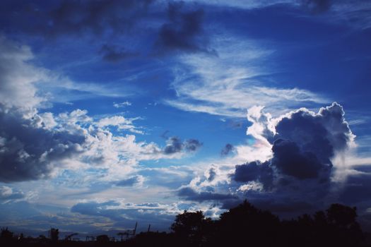 A captivating view of clouds over silhouetted trees against a vivid blue sky.