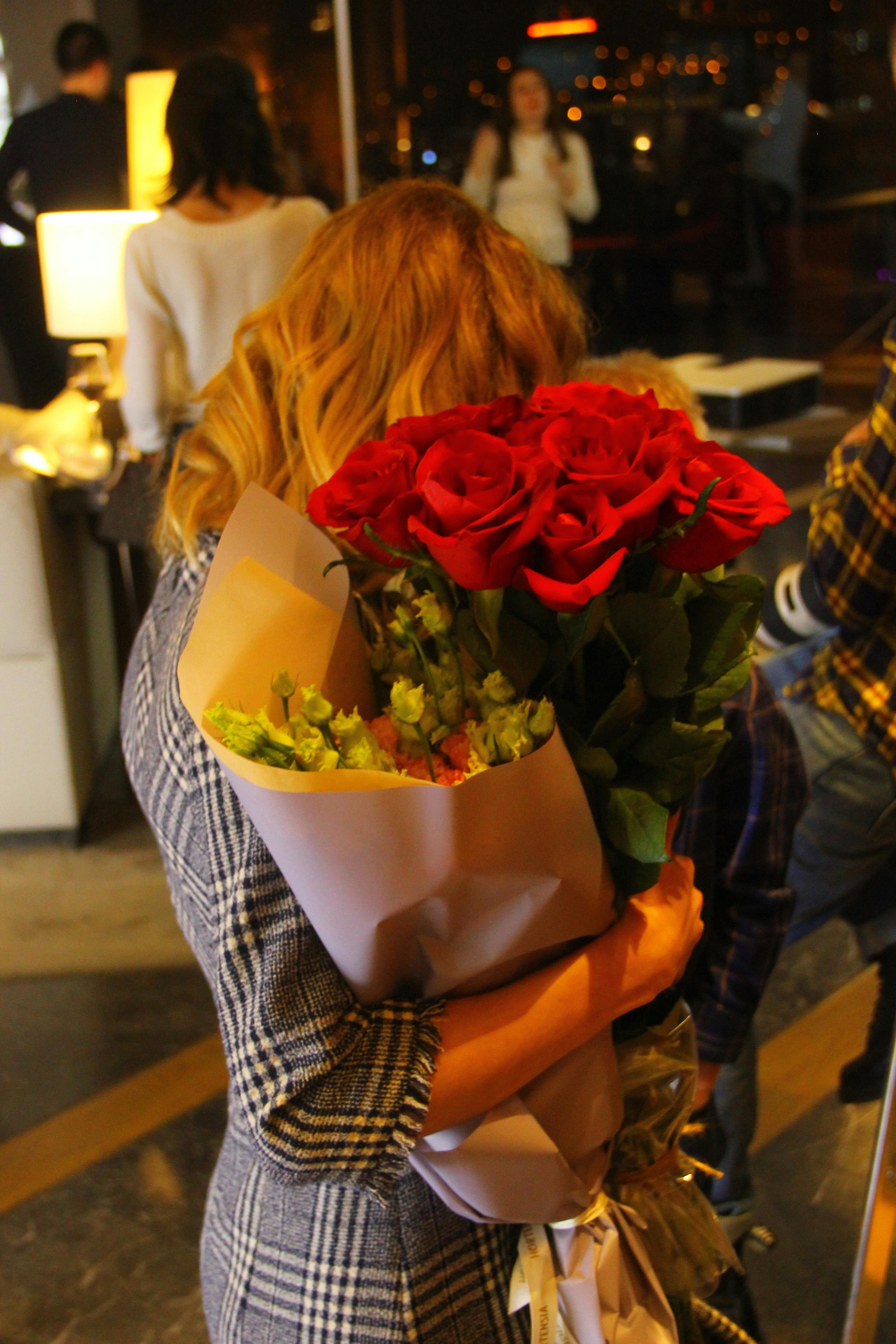Back view of a woman holding a bouquet of red roses inside, creating a warm and cozy atmosphere.