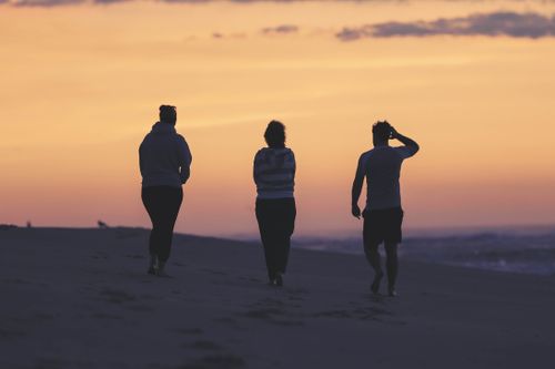 Free Three people walking on Beach Haven's shore during a vibrant sunset, enjoying tranquility. Stock Photo